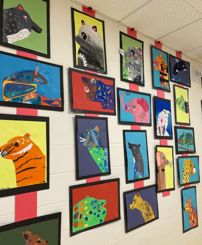 Middle school students hanging artwork together in a bright hallway exhibition.